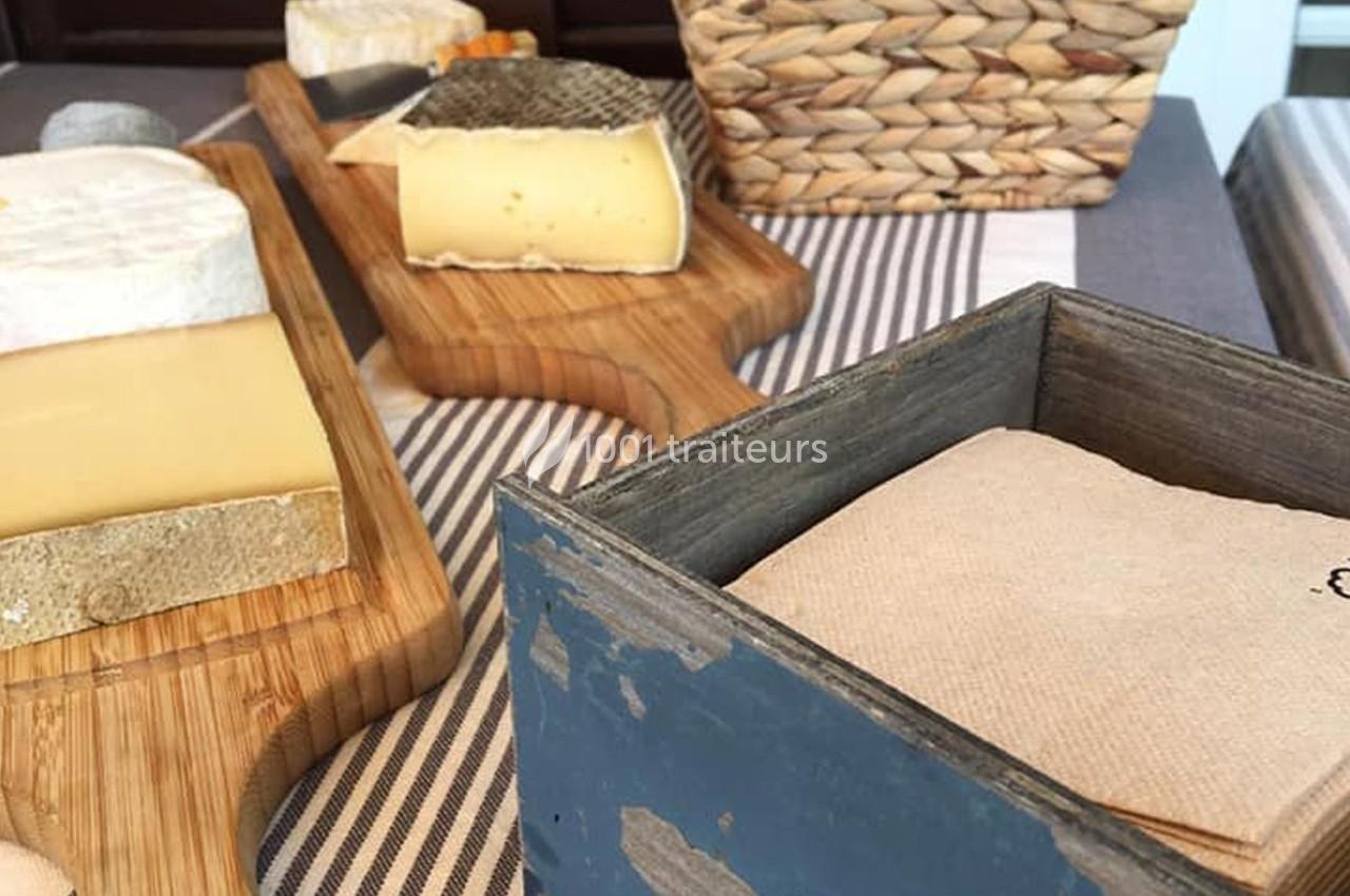 Plateau de fromages variés sur des planches en bois, avec une corbeille en osier et une boîte contenant des serviettes.