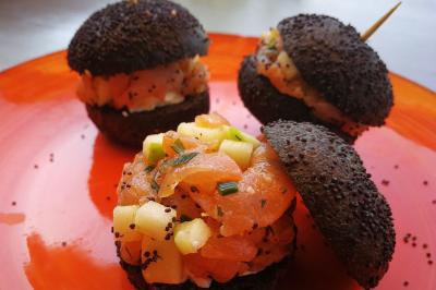 Bagels au sésame garnis de fromage frais, de légumes verts et d'herbes, disposés sur un plateau.