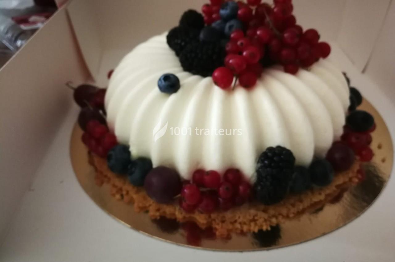 Gâteau blanc texturé décoré de fruits rouges, myrtilles et mûres, posé sur un disque doré.