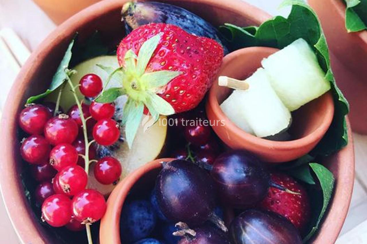 Bol en terre cuite contenant des fruits variés : fraises, groseilles, figues, prunes, melon et feuilles vertes.