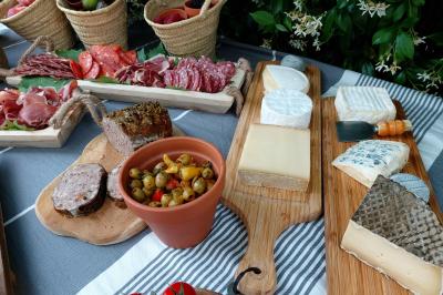 Plateau de fromages variés, charcuteries, olives et tomates cerises disposés sur une table avec nappes et paniers en arrière…