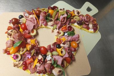 Couronne apéritive garnie de charcuterie, légumes, olives, tomates cerises et fleurs comestibles sur une planche.