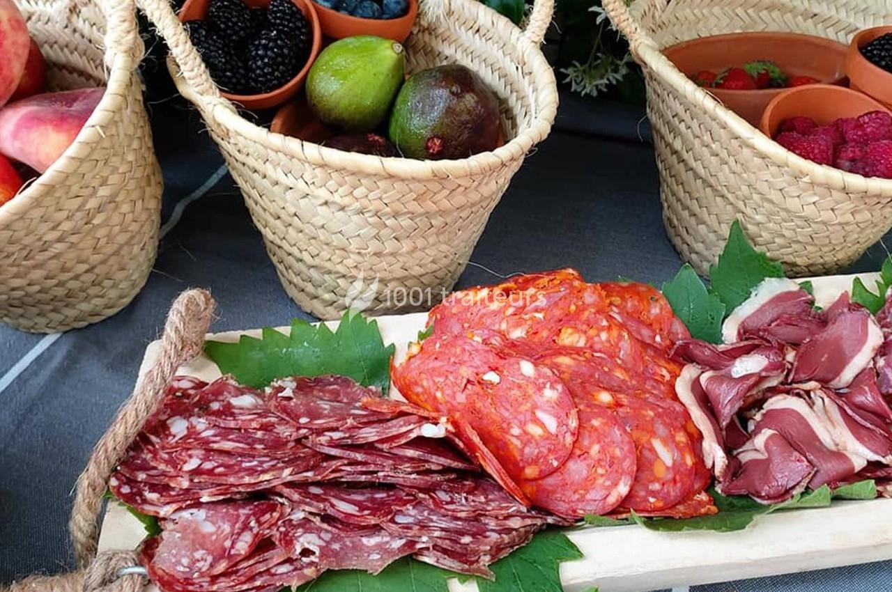 Plateau de charcuterie avec saucisson, chorizo et viande séchée, entouré de paniers de fruits frais.