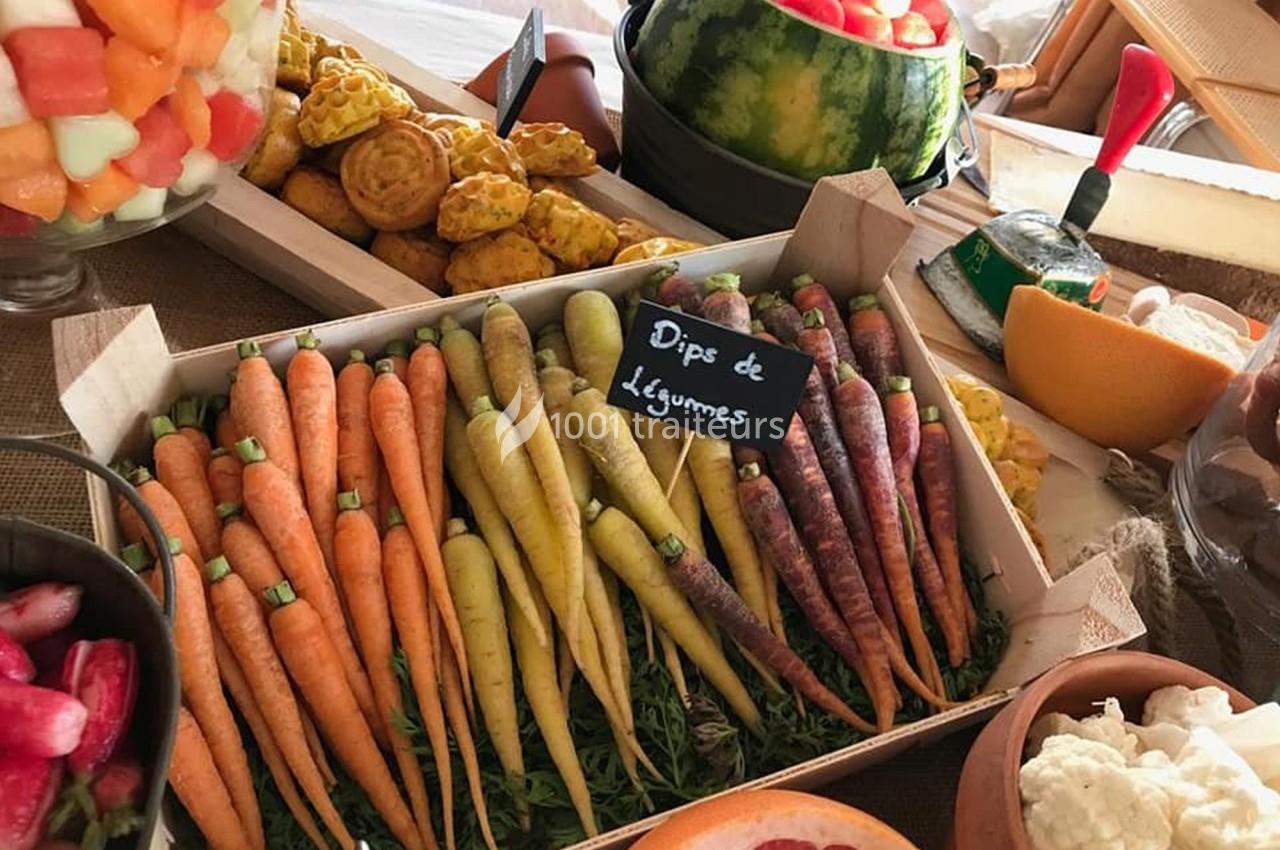 Plateau de carottes multicolores avec une étiquette ’Dips de Légumes’, entouré de fruits et autres aliments.