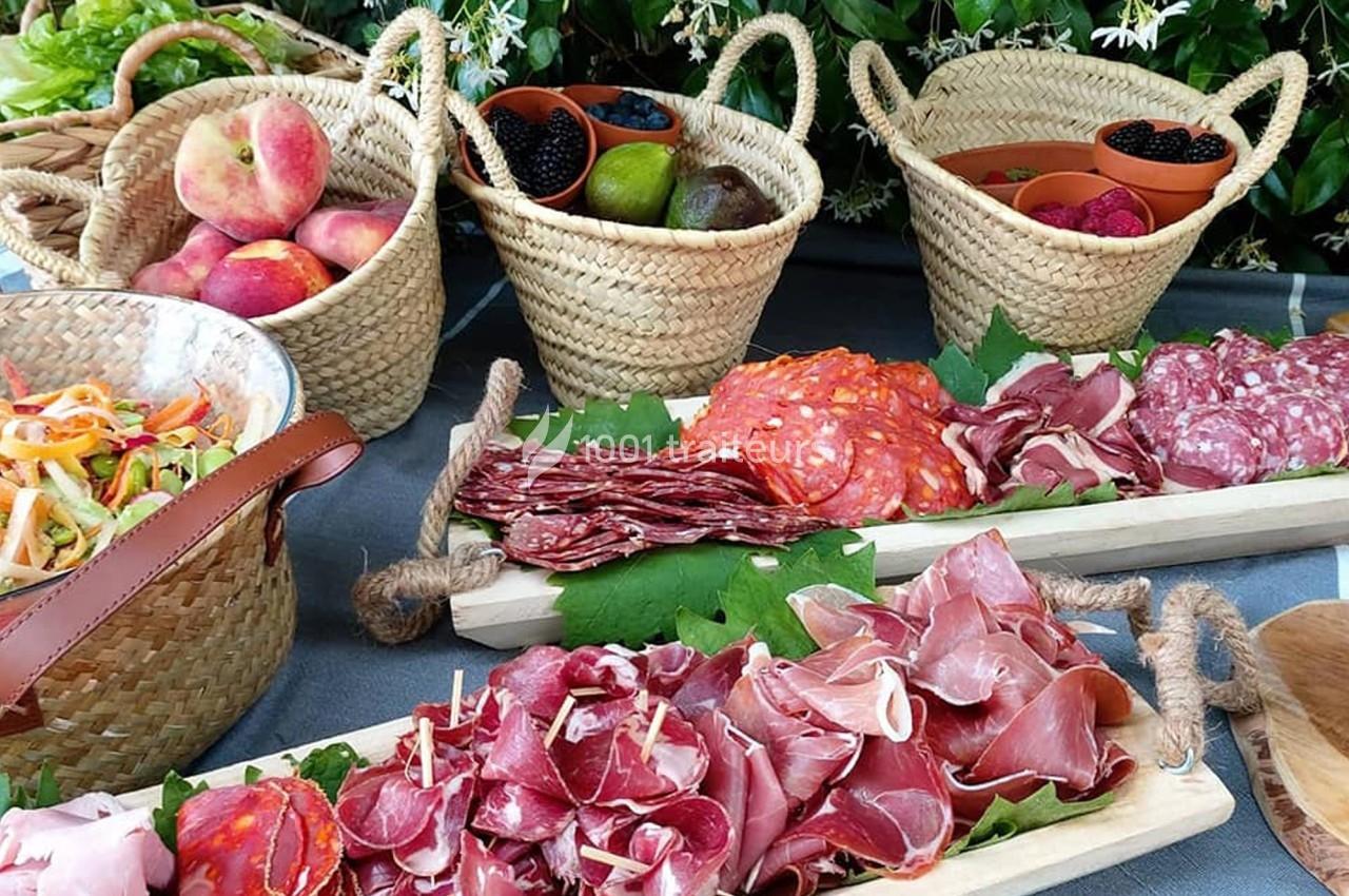 Plateaux de charcuterie variée et paniers de fruits frais disposés sur une table en extérieur.