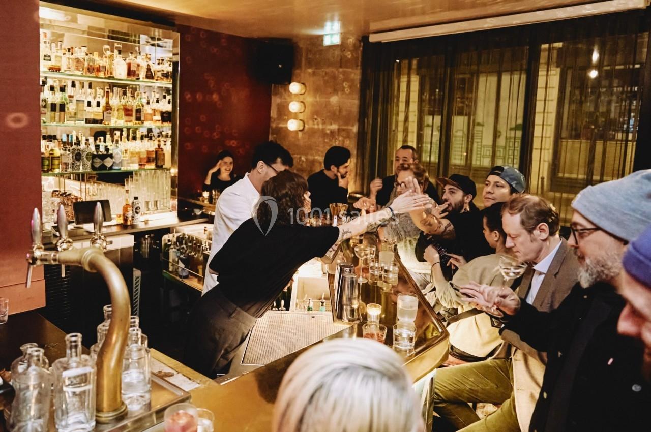 Un bar animé avec des clients discutant et un barman servant des boissons derrière le comptoir.