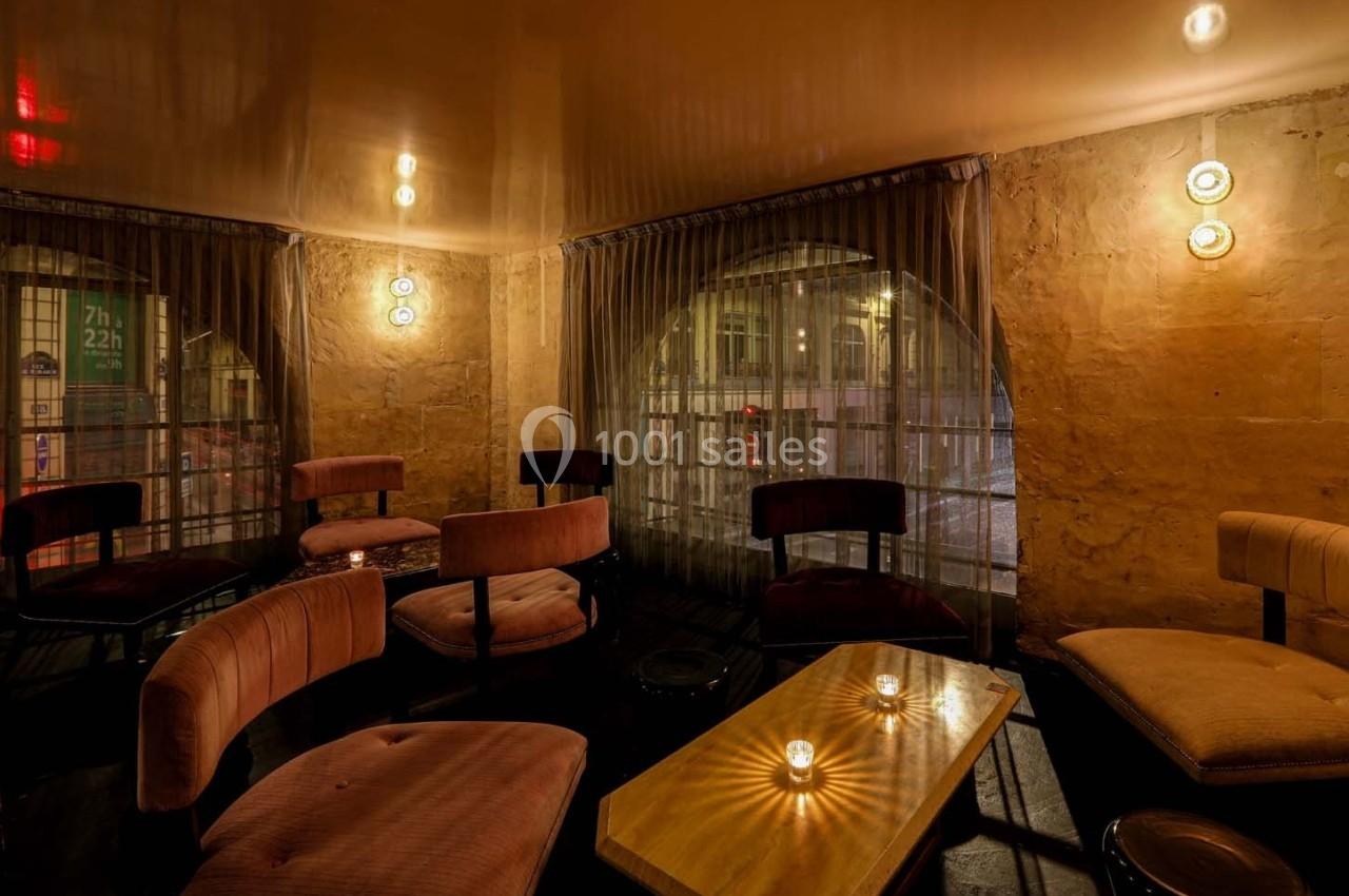 Espace intérieur chaleureux avec fauteuils, table basse en bois et bougies, éclairé par des lumières tamisées.