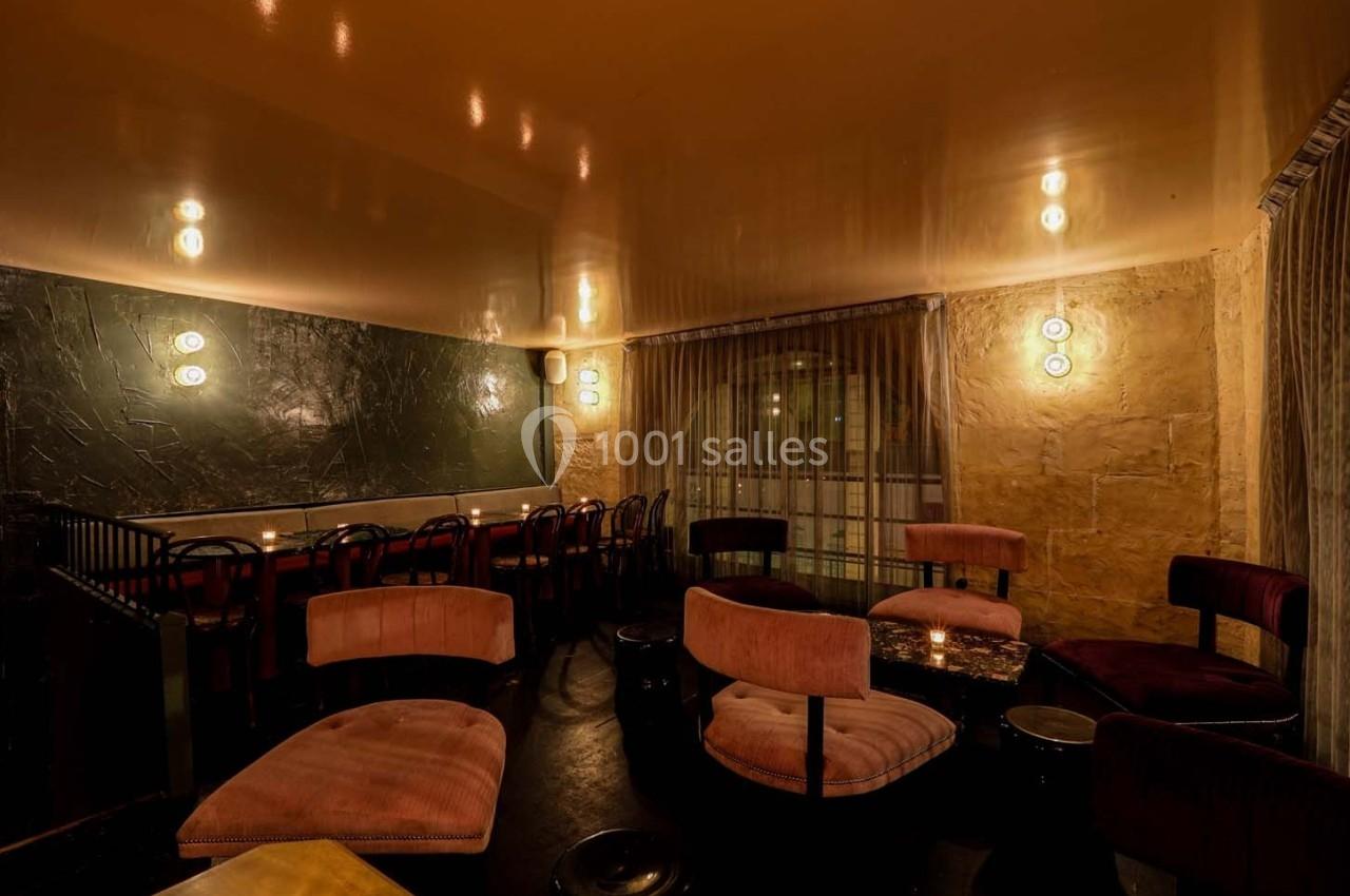 Salle de restaurant avec éclairage tamisé, murs en pierre, rideaux translucides et mobilier aux tons sombres et chauds.