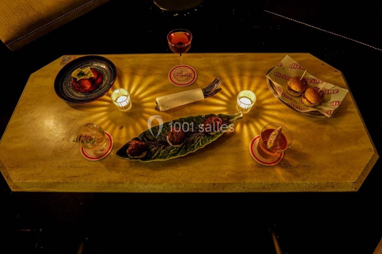 Table dressée avec des amuse-bouches, verres de boisson, bougies allumées et serviette pliée sur une nappe beige.
