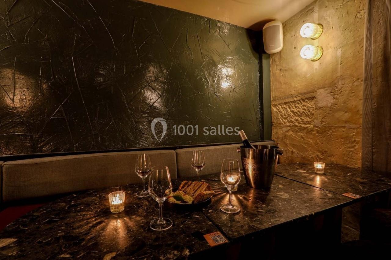 Table sombre avec des verres à vin, une assiette de nourriture et un seau à champagne, éclairée par des bougies.