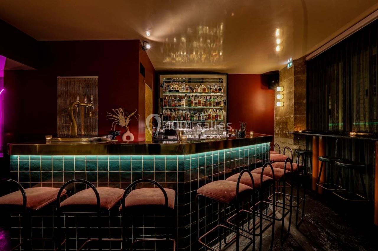 Bar élégant avec comptoir carrelé, tabourets rembourrés, étagères remplies de bouteilles et éclairage tamisé.