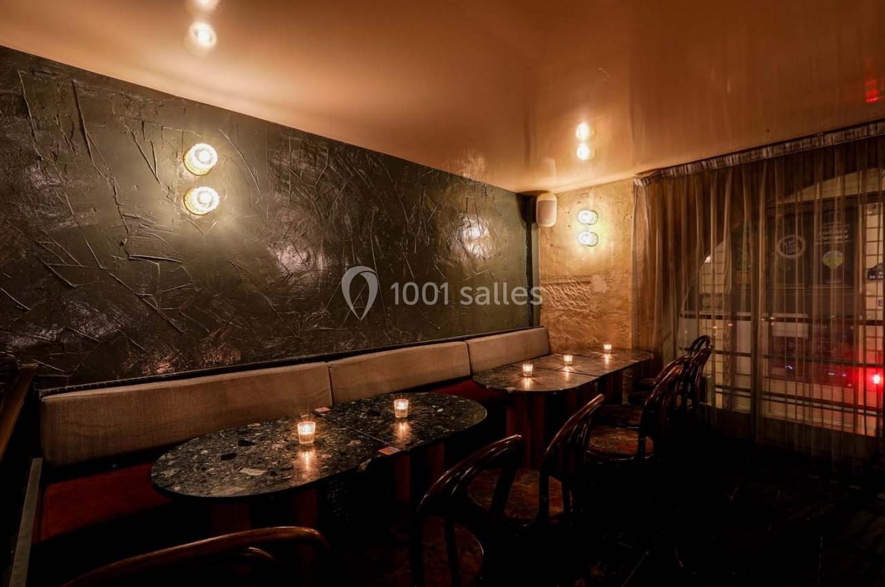 Salle de restaurant intimiste avec tables en marbre, banquettes, chaises en bois et éclairage tamisé.
