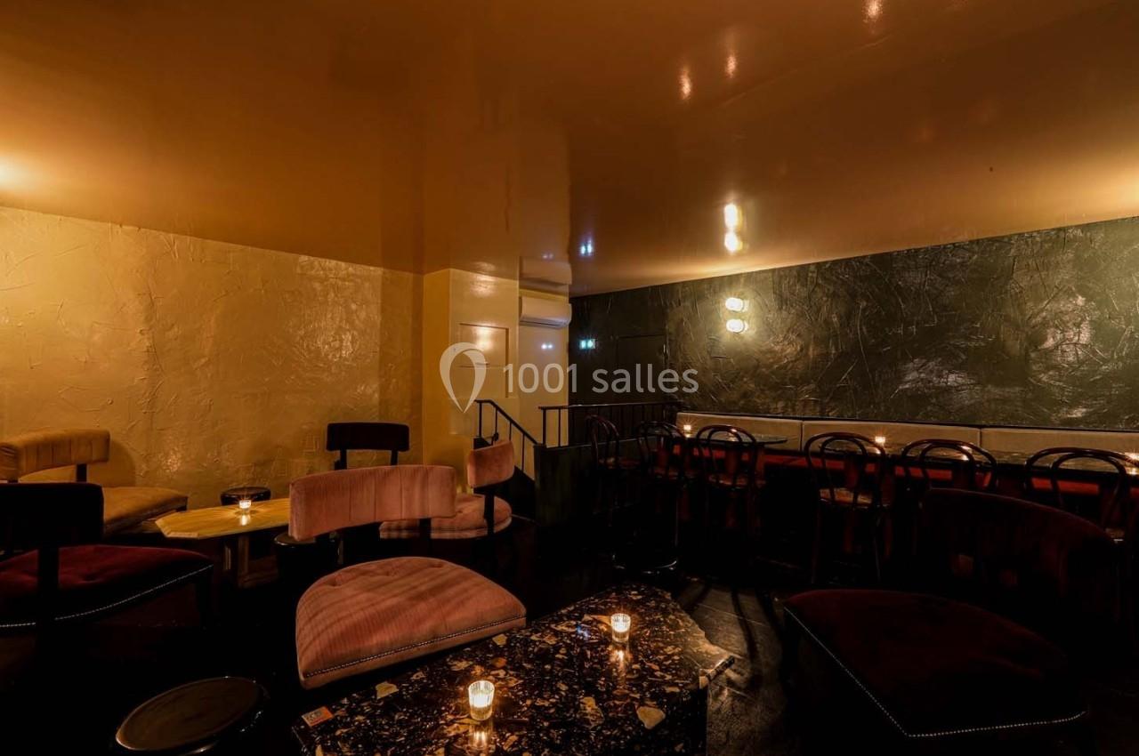Salle de bar tamisée avec des fauteuils en velours, des tables basses et des murs aux textures contrastées.