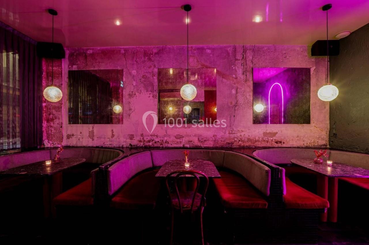 Salle de restaurant avec banquettes rouges, tables en marbre noir, éclairage tamisé et murs au style brut.