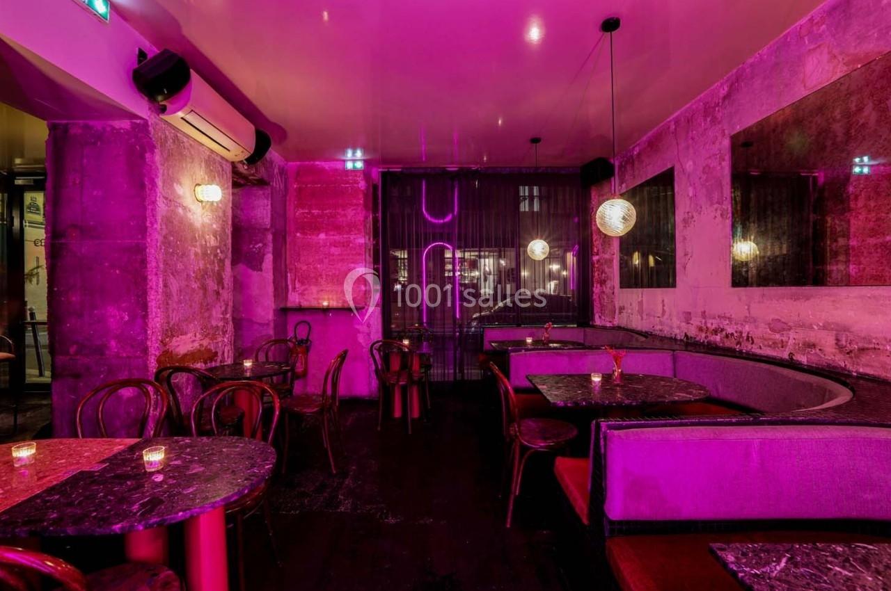 Salle de restaurant avec éclairage rose, tables en marbre, chaises en bois et banquettes contre un mur texturé.