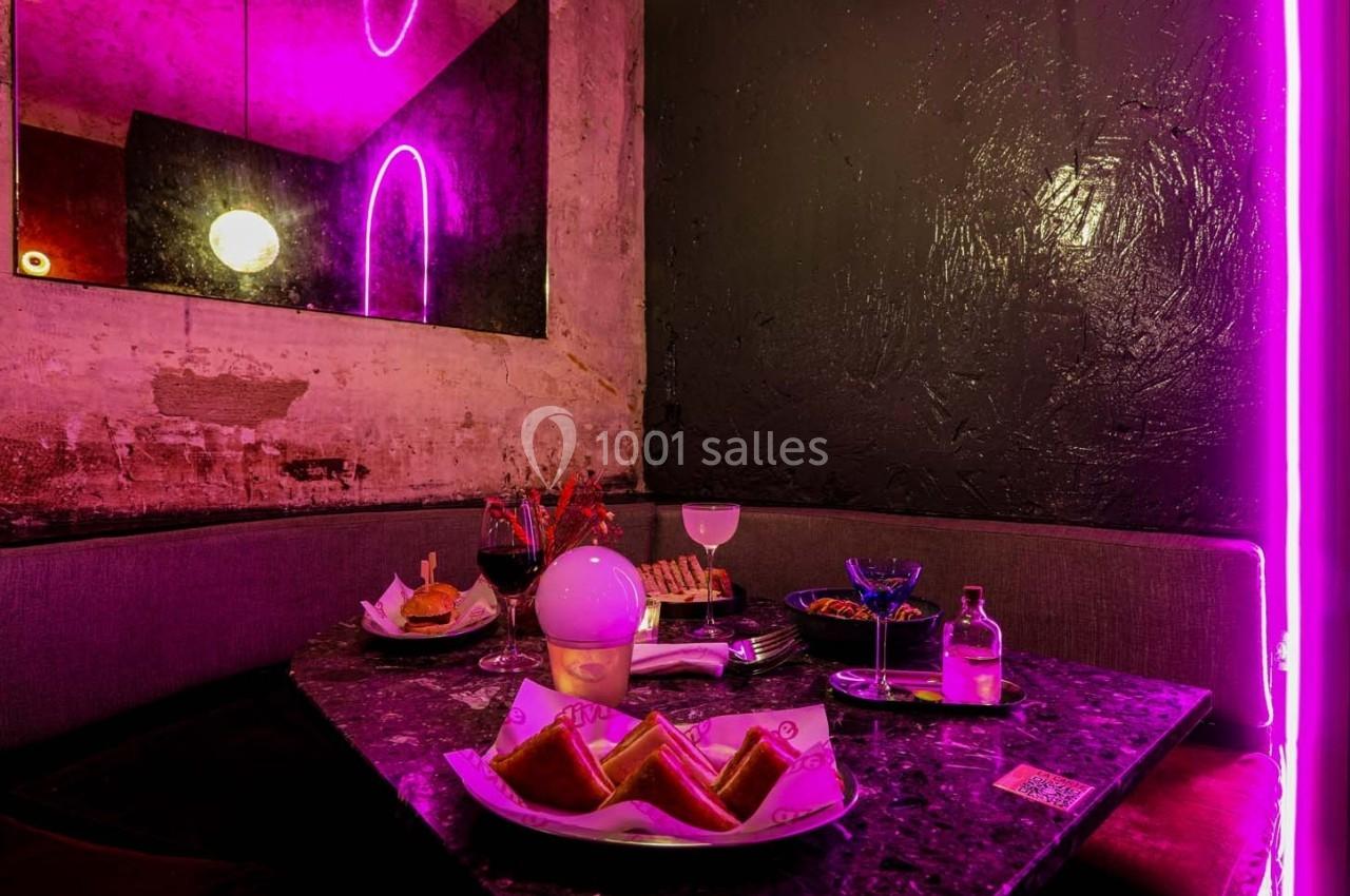 Banquette dans un décor néon avec table garnie de plats, cocktails et snacks sur une surface sombre.