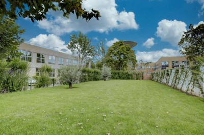 Parking vide entouré d'arbres et de bâtiments sous un ciel bleu avec quelques nuages.