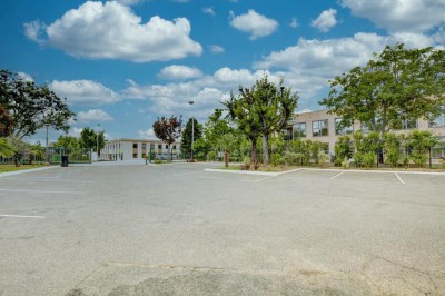 Parking vide entouré d'arbres et de bâtiments sous un ciel bleu avec quelques nuages.