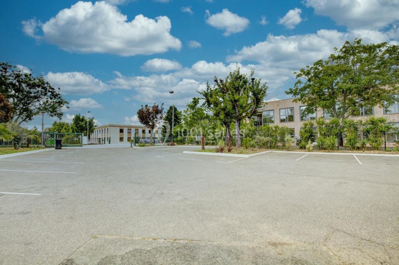 Parking vide entouré d'arbres et de bâtiments sous un ciel bleu avec quelques nuages.