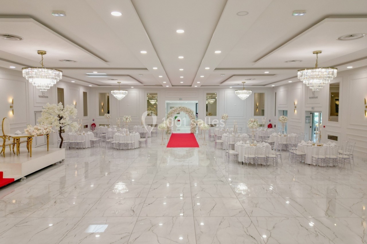 Salle de réception élégante avec sol en marbre, tables décorées, chandeliers et tapis rouge menant à une arche florale.