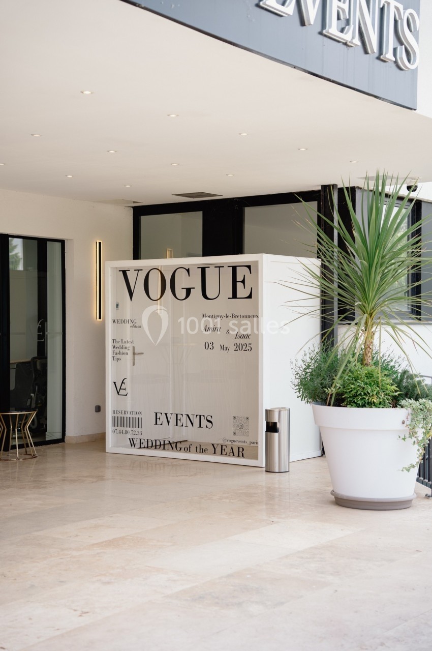 Une affiche de style magazine ’Vogue’ exposée devant un bâtiment moderne avec des plantes en pot.