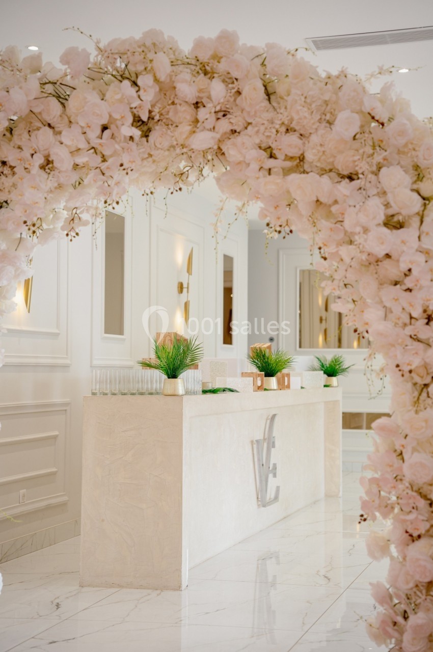 Arche de fleurs roses encadrant un comptoir élégant dans un intérieur lumineux avec décorations végétales.