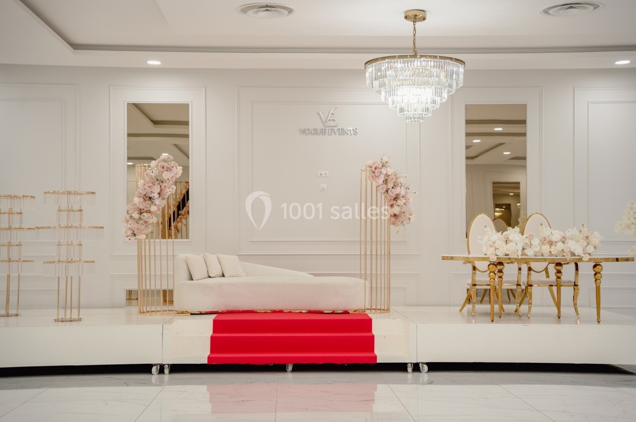 Salle élégante avec canapé blanc, table dorée décorée de fleurs et lustre en cristal, sur fond de murs blancs.