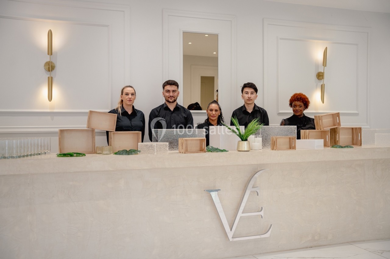 Cinq personnes en tenue noire debout derrière un comptoir décoré de plantes et d'éléments en bois et verre.