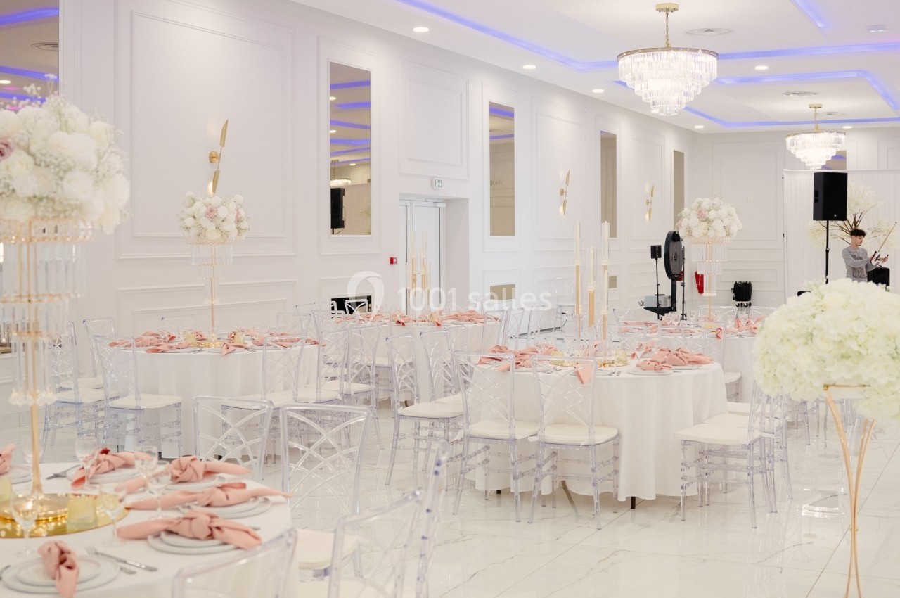 Salle de réception élégante avec tables rondes dressées, nappes blanches, serviettes roses et décorations florales.