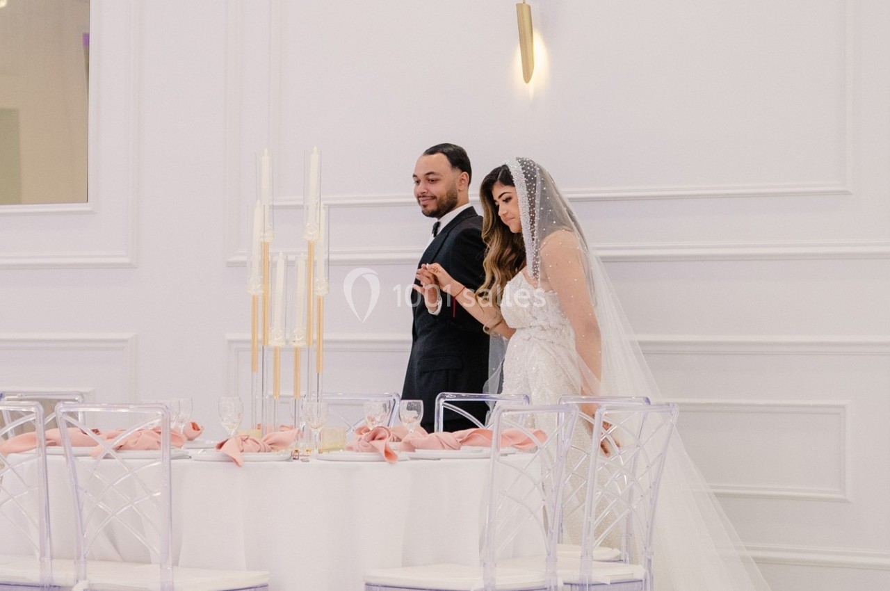 Un couple en tenue de mariage marche près d'une table décorée avec des serviettes roses et des chandeliers.