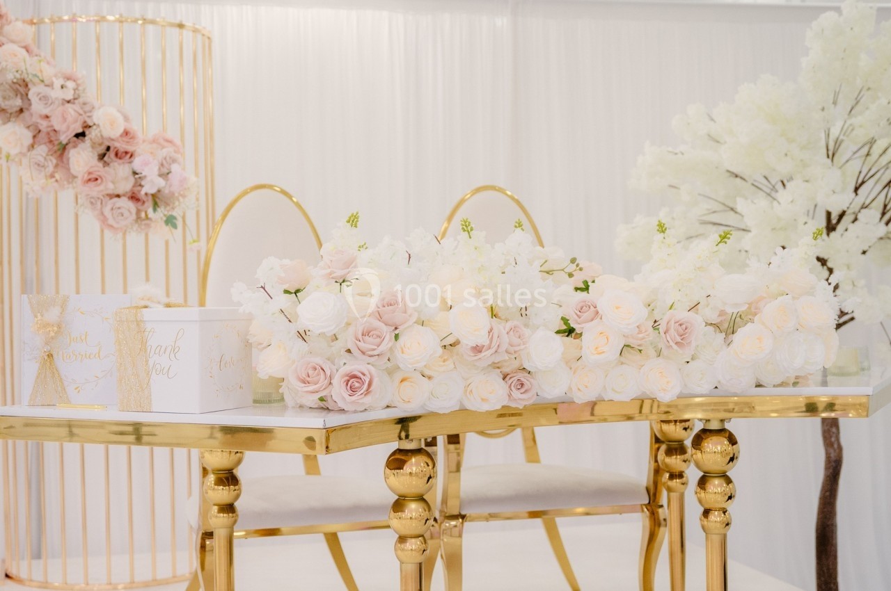 Table décorée avec des bouquets de roses blanches et roses, entourée de chaises dorées et d'éléments floraux.