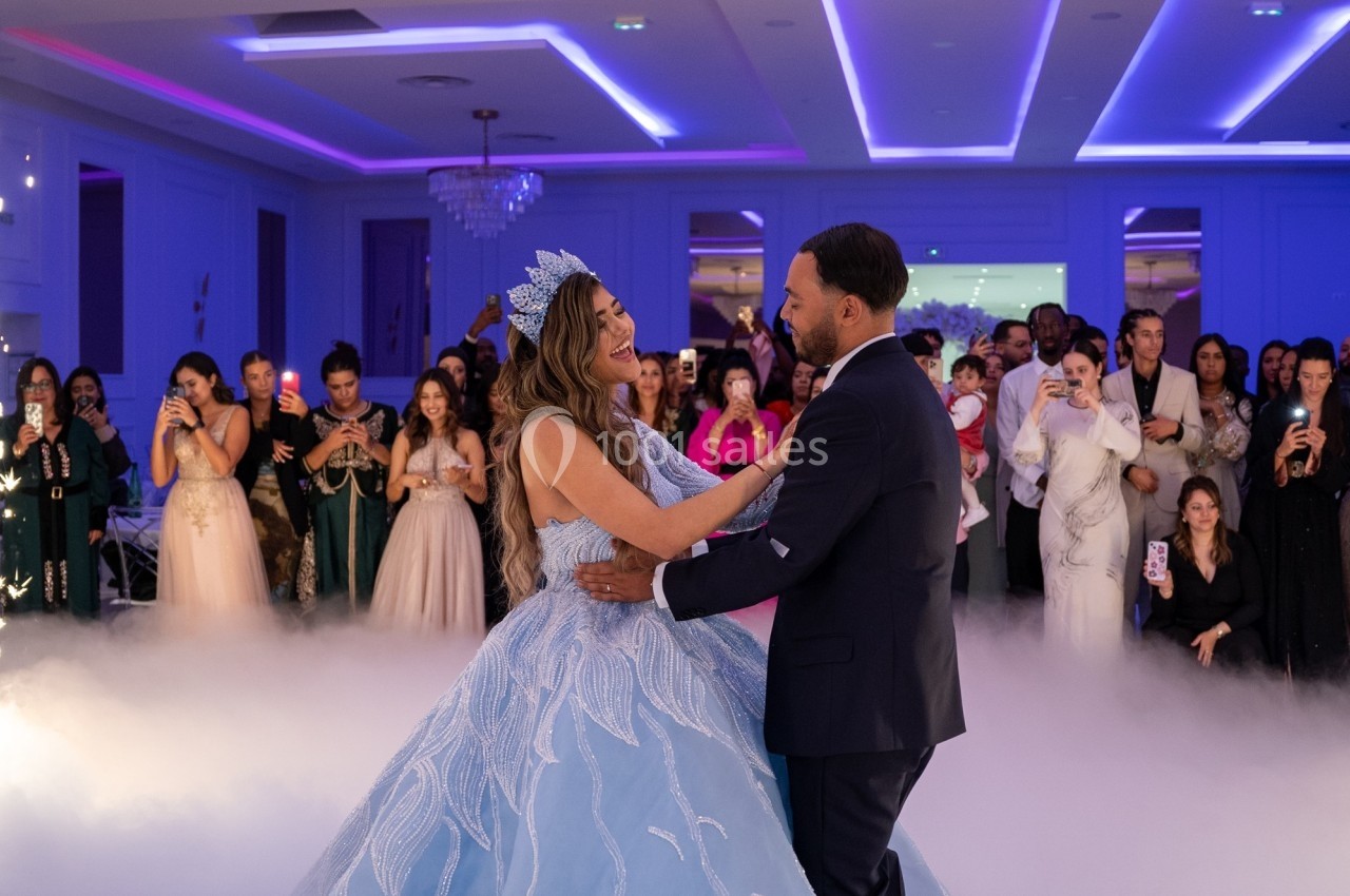 Un couple danse sous des lumières violettes, entouré d'invités élégants dans une salle de réception.