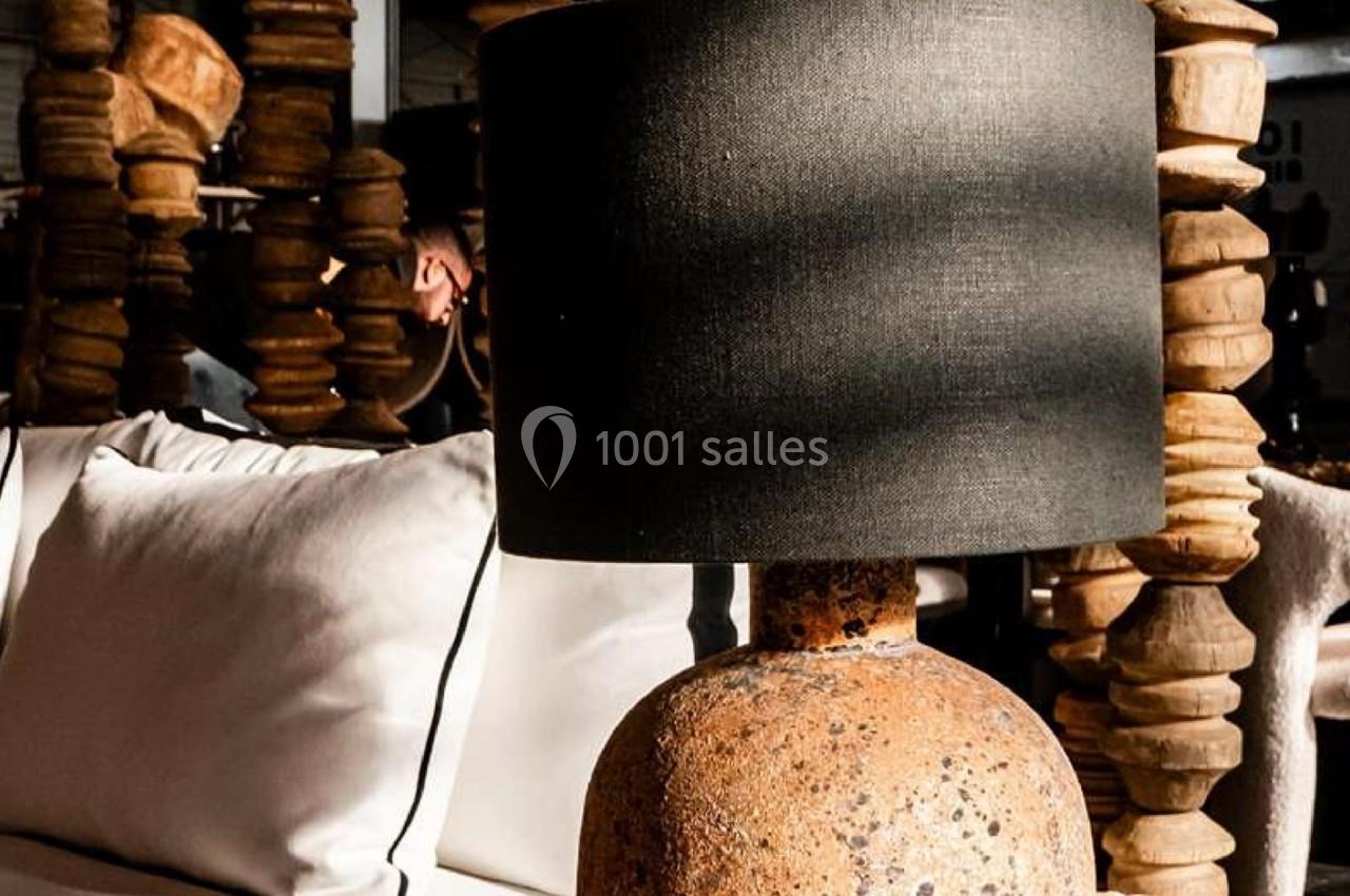 Lampe à abat-jour noir sur une base en pierre texturée, posée sur une table près de coussins blancs et de colonnes en bois.