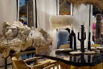 Sculpture de lion en pierre, table en bois sombre avec chandeliers noirs, vase bleu et décor rustique en arrière-plan.