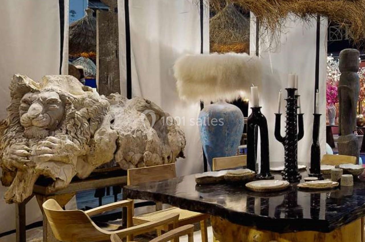 Sculpture de lion en pierre, table en bois sombre avec chandeliers noirs, vase bleu et décor rustique en arrière-plan.