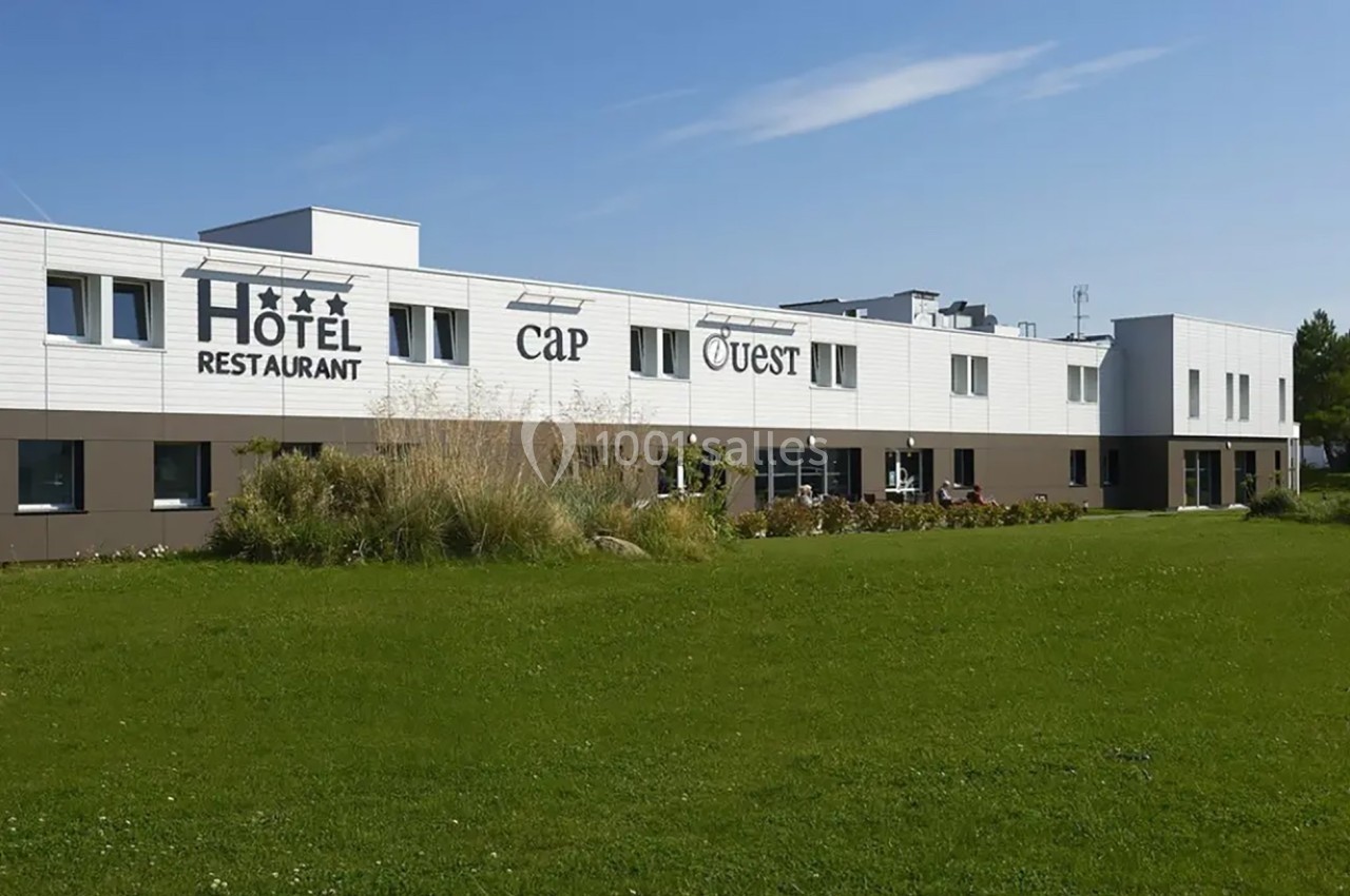 Façade d'un hôtel-restaurant moderne à un étage, entouré de pelouse et de végétation sous un ciel dégagé.