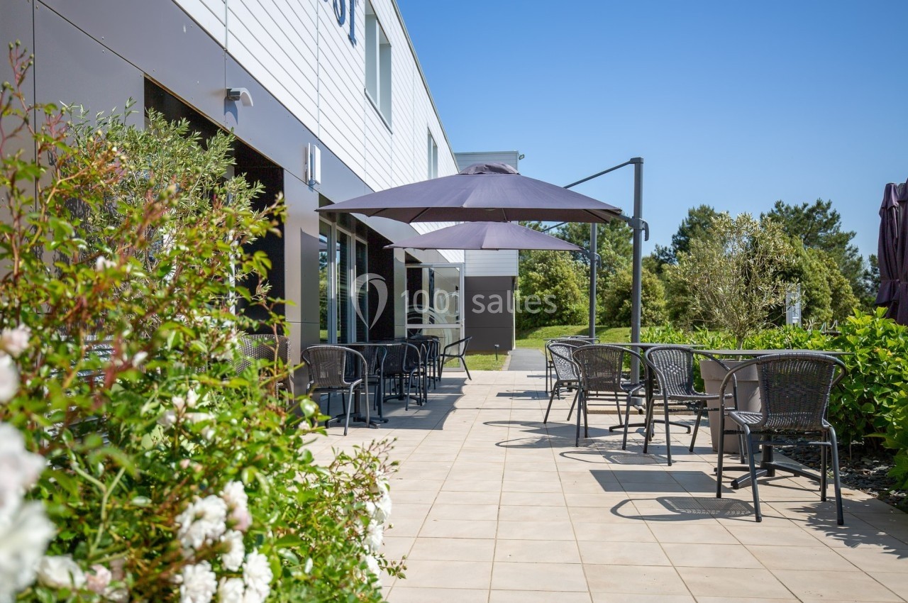 Terrasse extérieure avec tables, chaises et parasols, entourée de végétation et baignée de lumière naturelle.