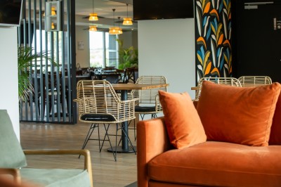 Espace intérieur lumineux avec des fauteuils en rotin, une table en bois et une décoration murale colorée.