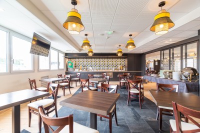 Espace intérieur lumineux avec des fauteuils en rotin, une table en bois et une décoration murale colorée.