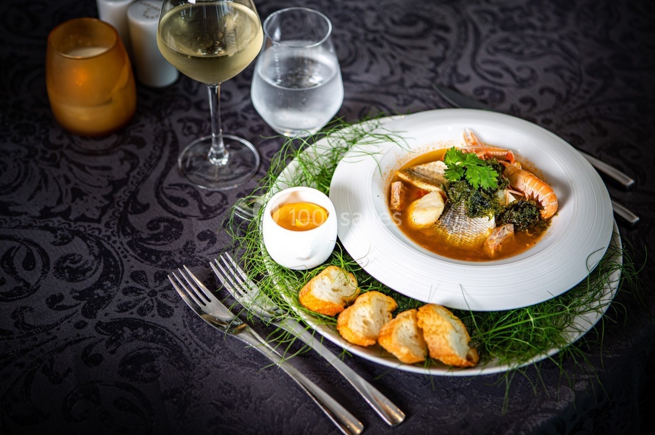 Assiette de bouillabaisse avec poissons, crustacés, croûtons, sauce et verres de vin et d'eau sur une table sombre.