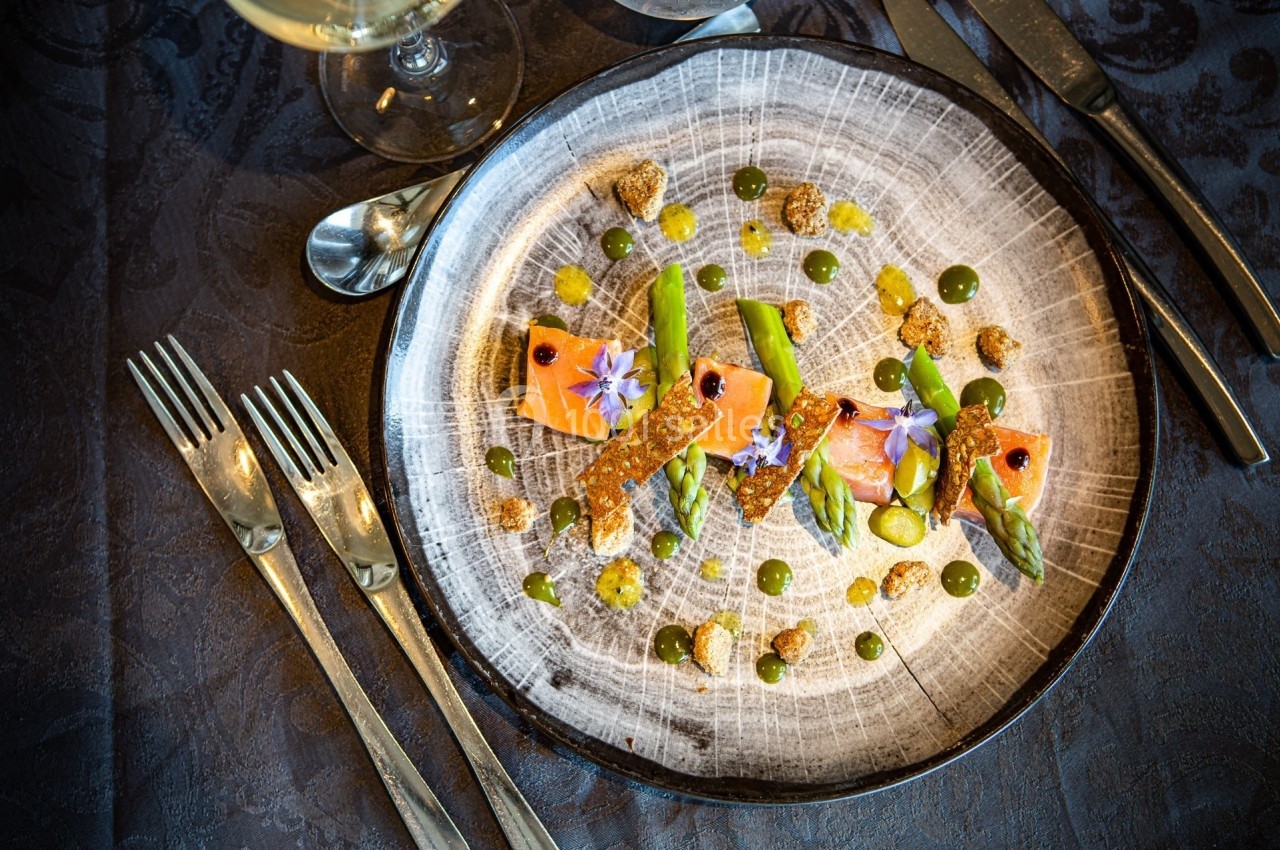 Assiette gastronomique avec saumon, asperges, fleurs comestibles et sauces décoratives sur une table sombre.