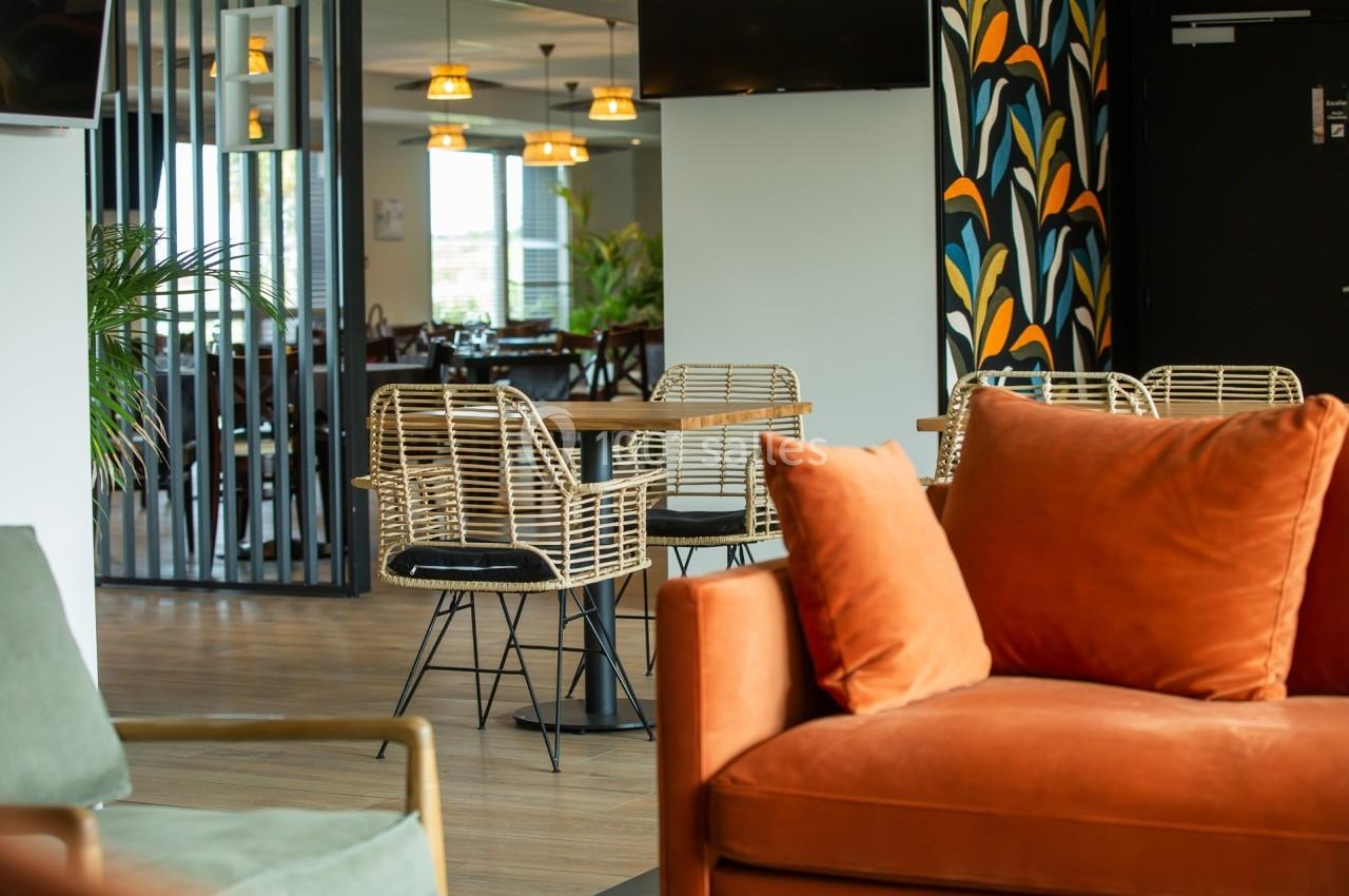 Espace intérieur avec fauteuils colorés, tables en bois et chaises en rotin, décoré de motifs muraux et plantes.