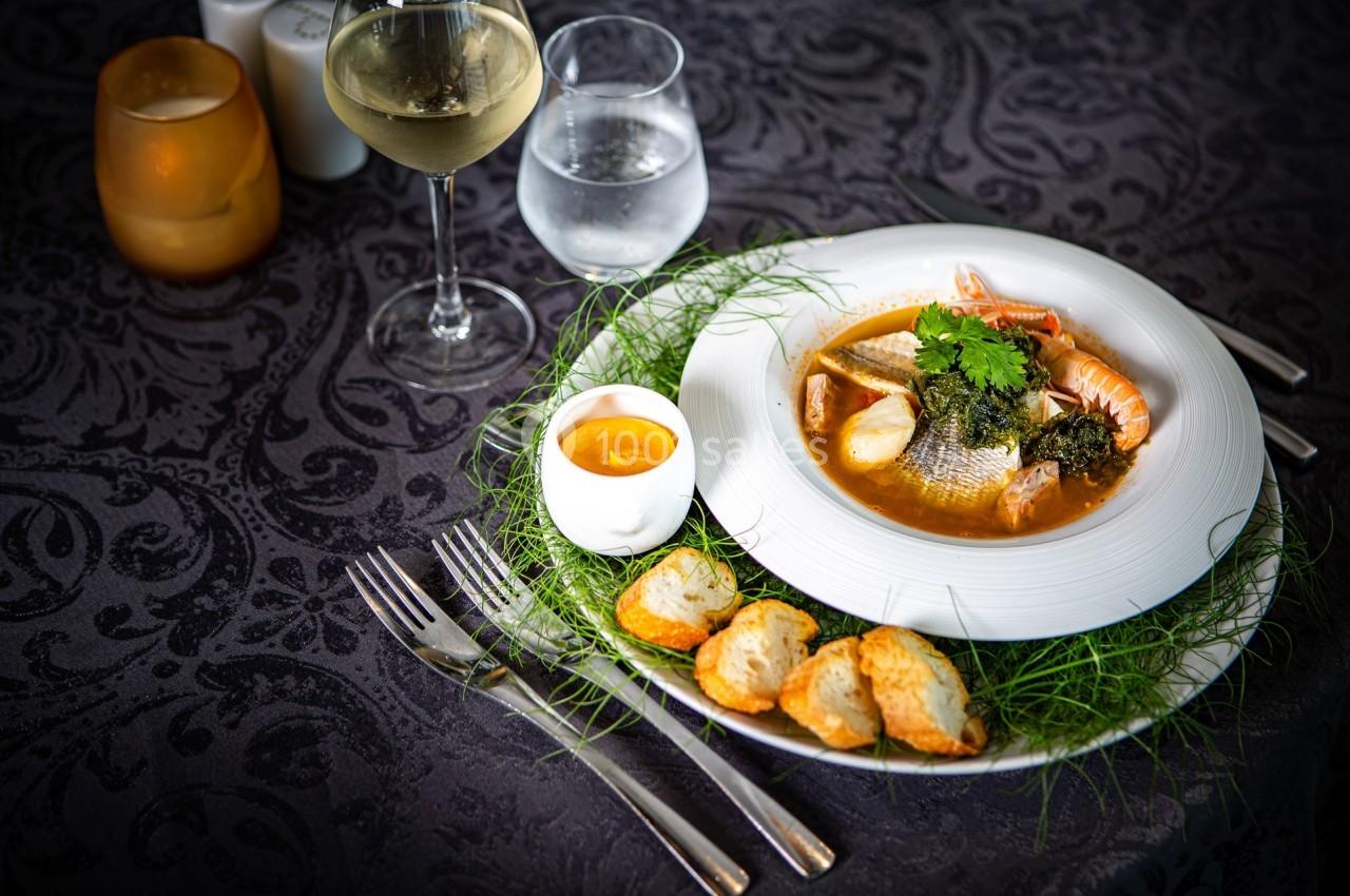 Assiette de soupe de poisson garnie de fruits de mer, accompagnée de croûtons, sauce et verres d'eau et de vin.