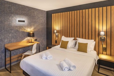 Chambre d'hôtel moderne avec lit double, bureau, téléviseur mural, portant, et décoration murale à motifs floraux.