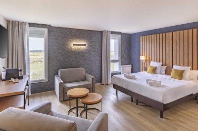 Chambre d'hôtel moderne avec lit double, bureau, téléviseur mural, portant, et décoration murale à motifs floraux.