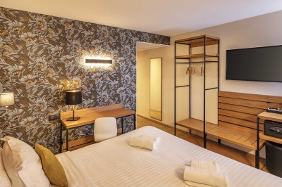 Chambre d'hôtel moderne avec lit double, bureau, téléviseur mural, portant, et décoration murale à motifs floraux.
