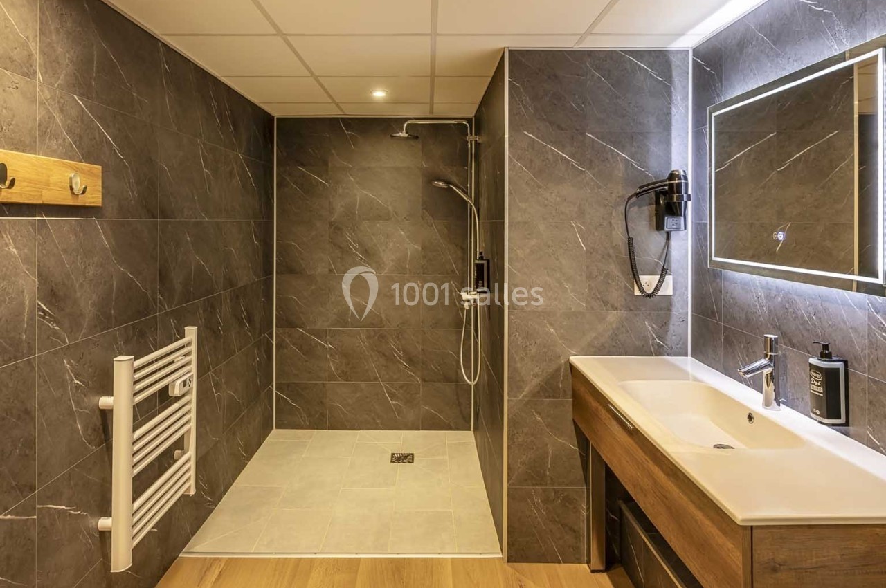 Salle de bain moderne avec douche à l'italienne, lavabo en bois, miroir éclairé et murs en carrelage gris foncé.