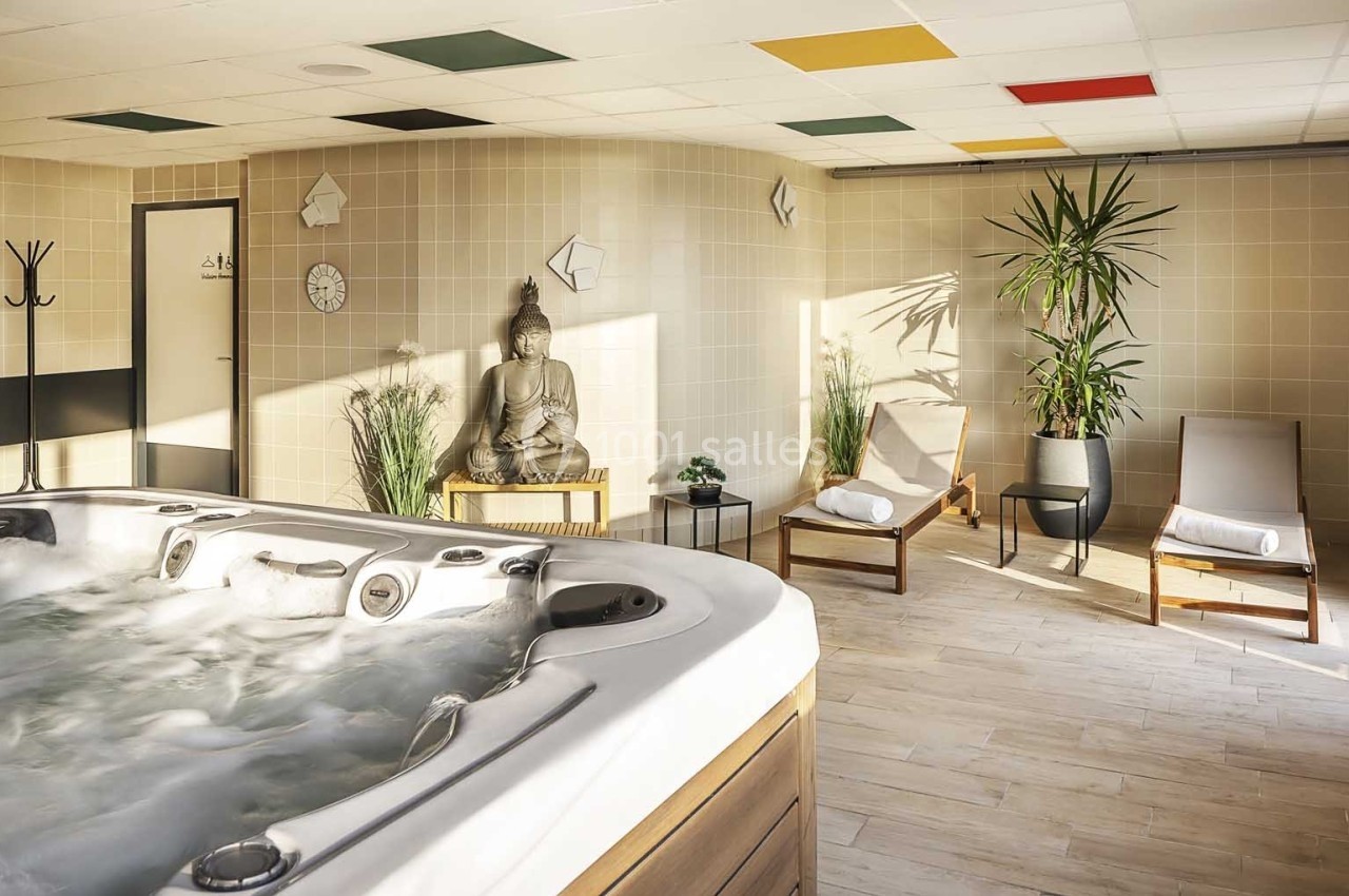 Salle de spa avec jacuzzi, statue de Bouddha, chaises longues, plantes et lumière naturelle.