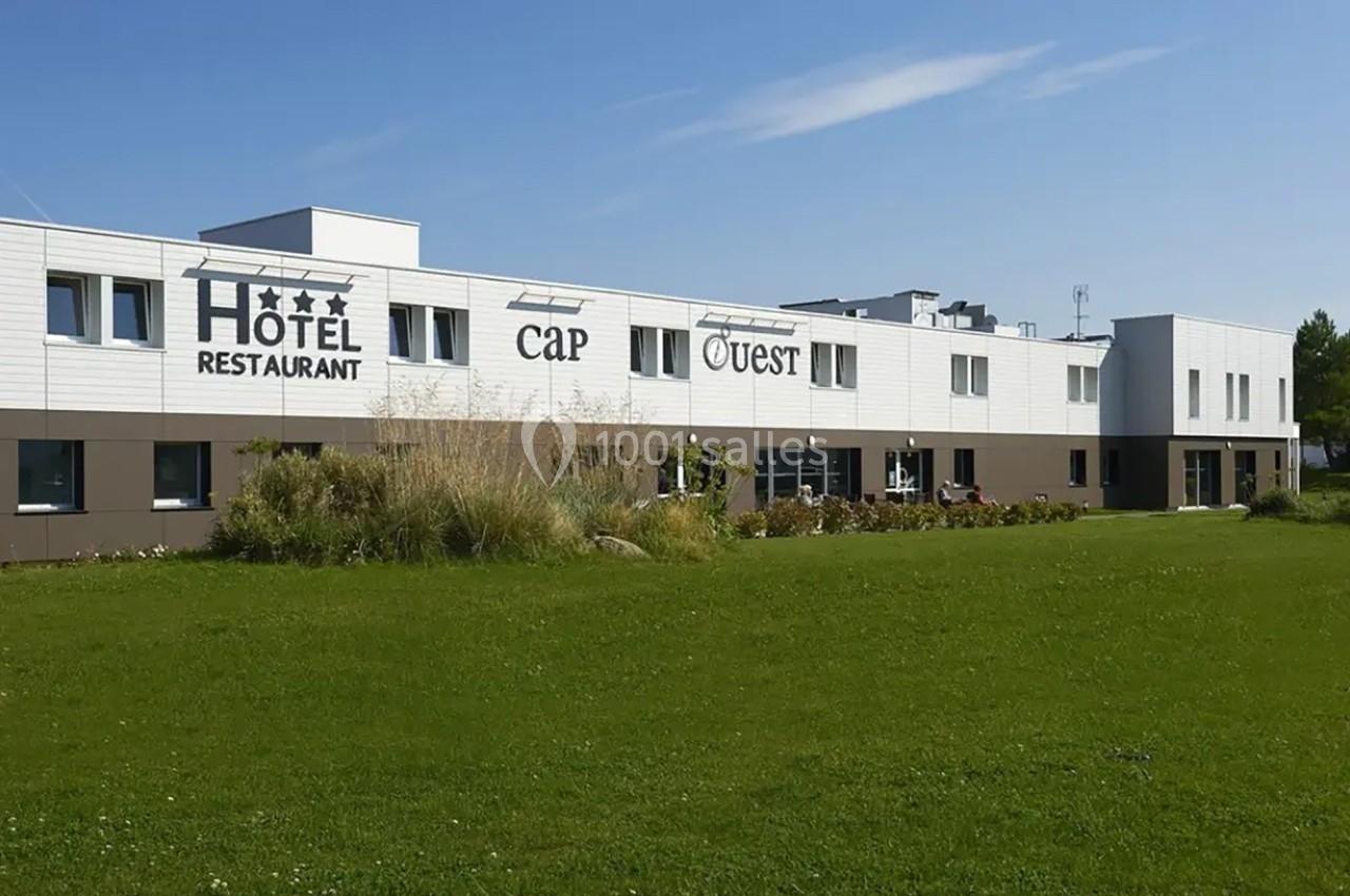 Façade d'un hôtel-restaurant moderne à deux étages, entouré de pelouse et de végétation sous un ciel dégagé.
