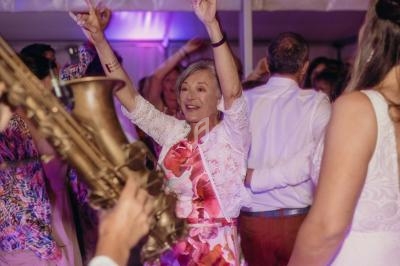 Une femme souriante danse lors d'une fête, entourée d'autres personnes et d'un saxophoniste au premier plan.
